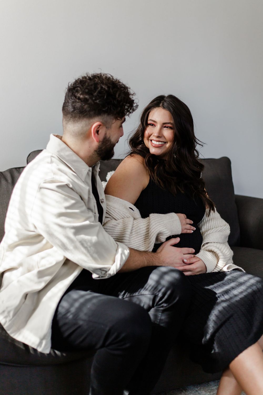 A couple sitting on a gray couch share intimate moments in a sequence of candid photographs.