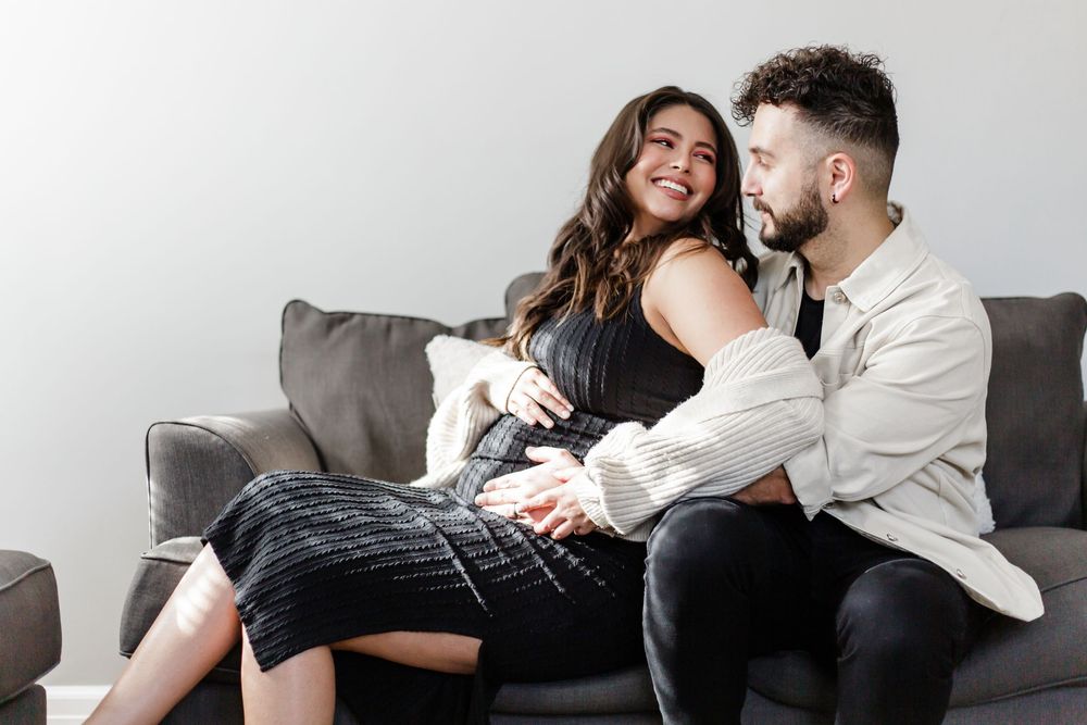 A couple relaxes on a grey couch together while laughing and enjoying each other's company.
