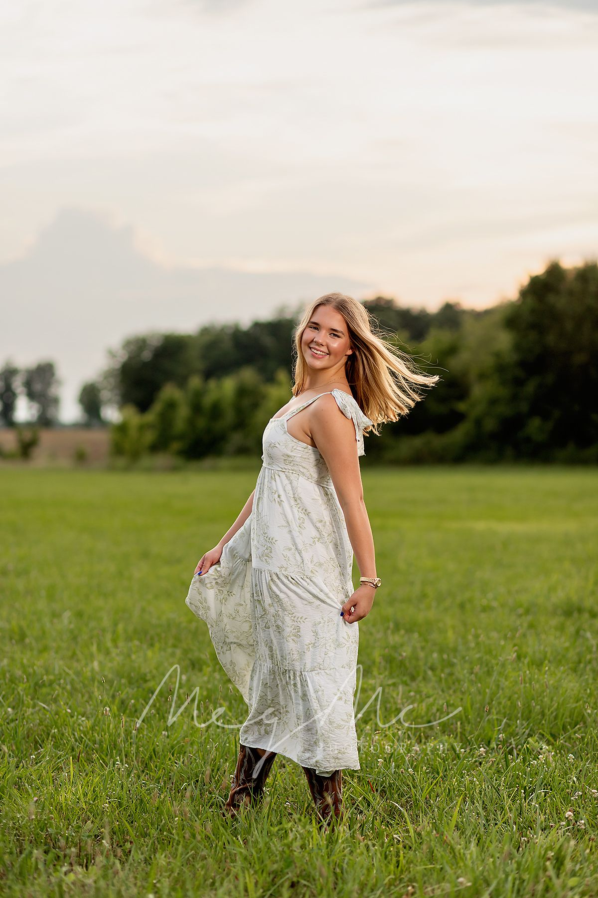 Teen in flowing white dress twirling joyfully in a sunlit meadow at sunset. Senior pictures with MegMc Photography, Medina, TN.