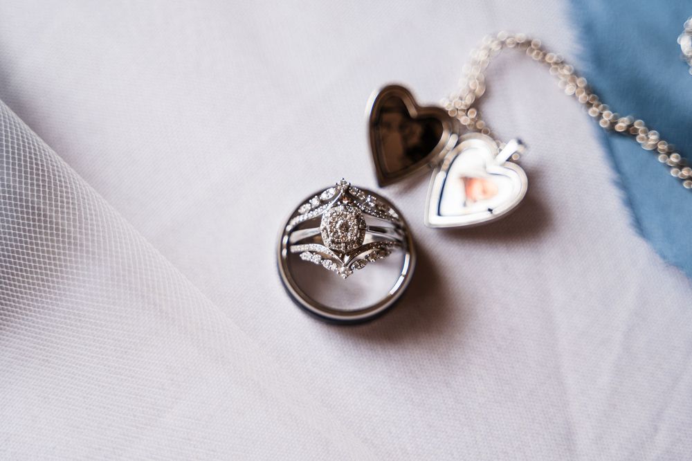 Delicate wedding rings and jewelry arranged on white fabric with soft lighting.