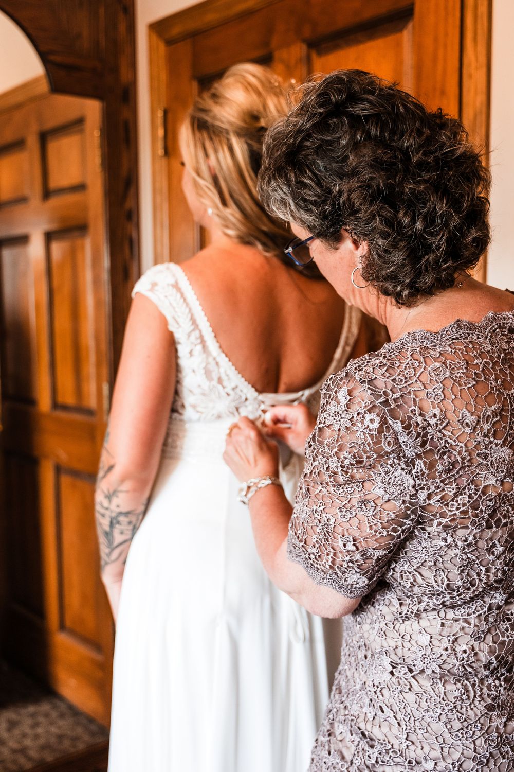 An elegant white wedding dress being buttoned up in preparation for the ceremony.