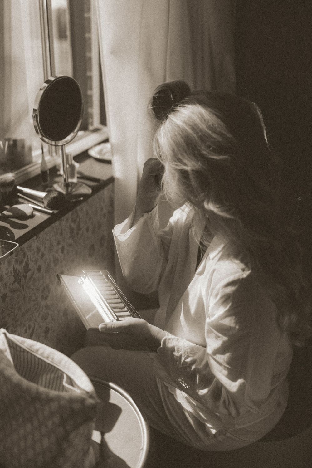 A black and white vintage photograph shows someone in white clothing sitting at a vanity with a makeup mirror and keyboard.