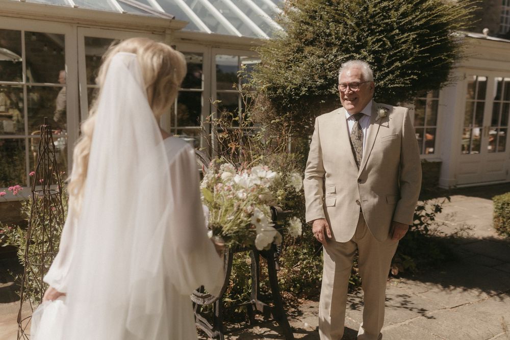 A bride and groom stand in a sunny courtyard under white columns during an outdoor garden wedding ceremony.