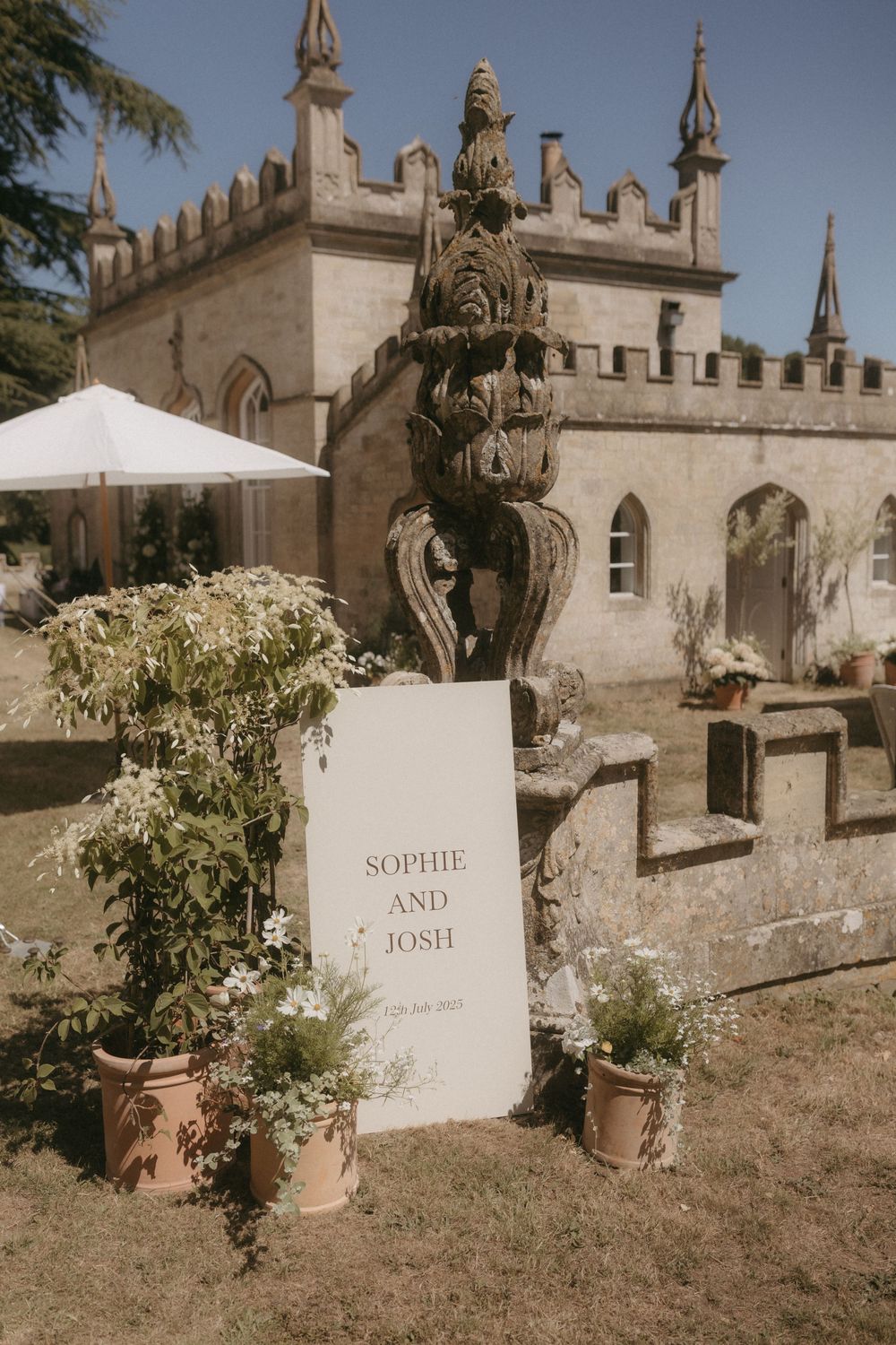 A rustic wedding sign for Sophie and Josh displayed in front of a gothic castle with ornate spires and arches.