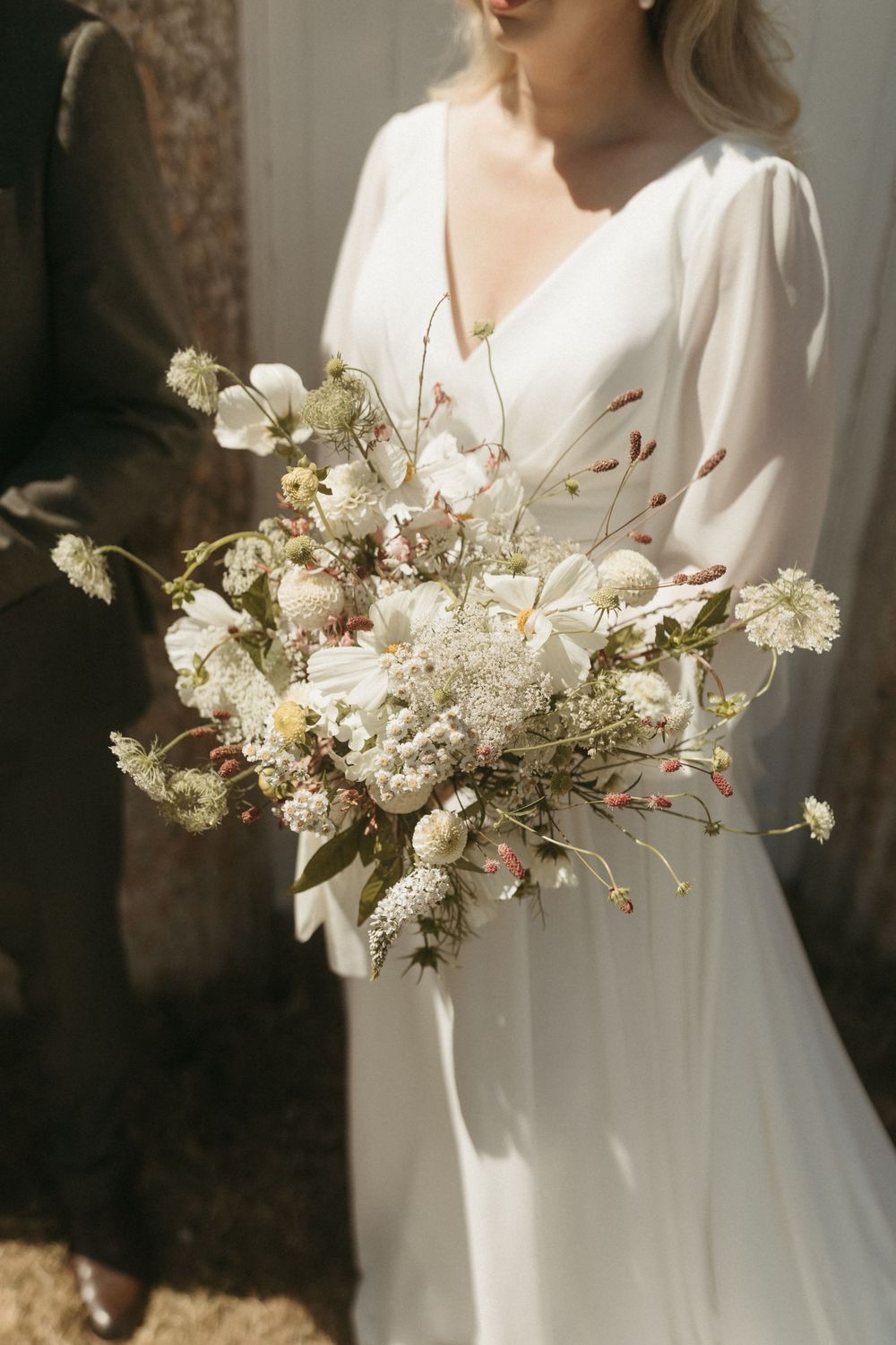 Elegant white wedding bouquet with dried flowers held by someone wearing a flowing white dress with puff sleeves.