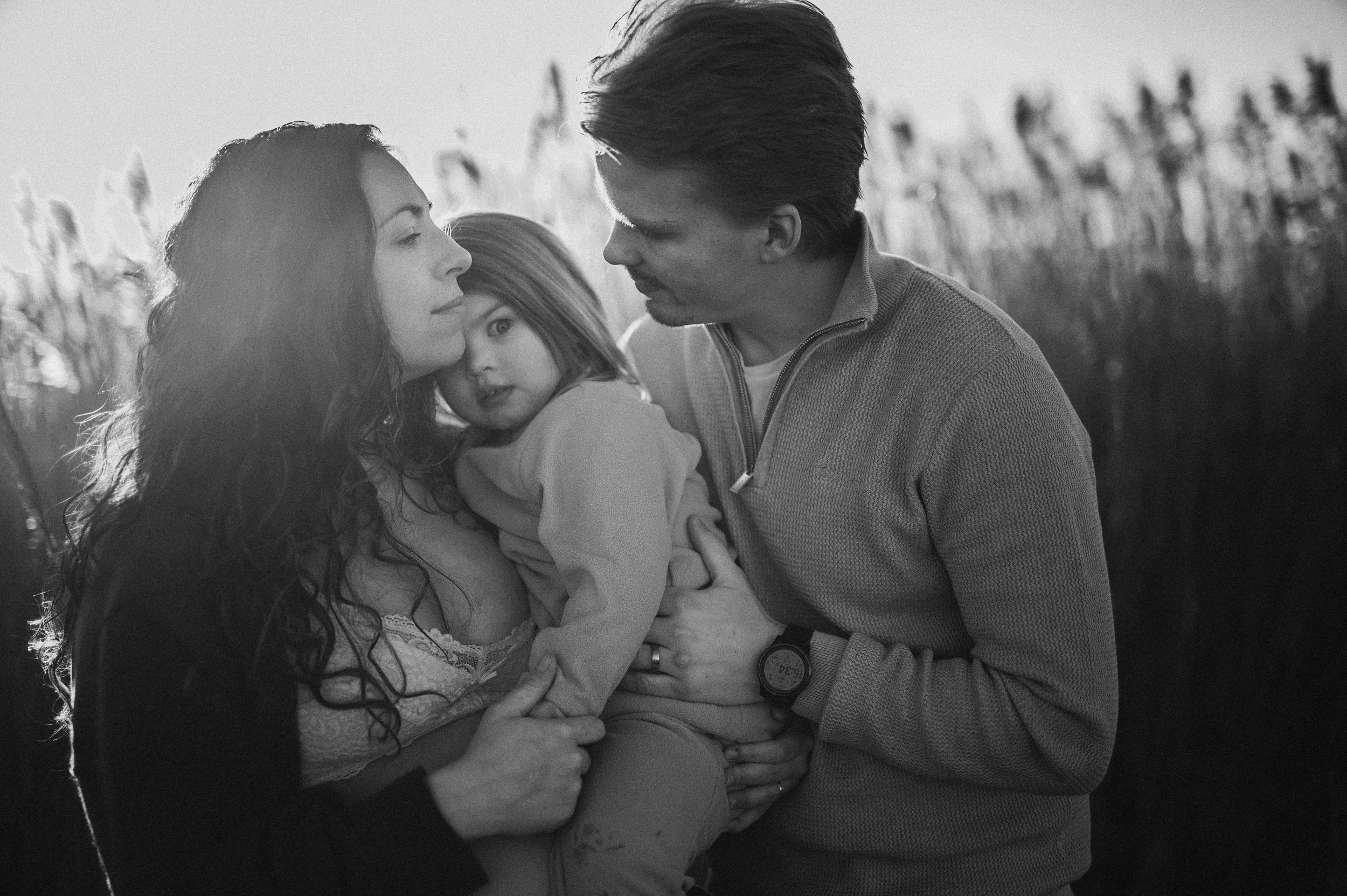 Svartvitt familjeögonblick i kvällsljus – fångat i högt gräs under golden hour i Skåne nära Hässleholm.