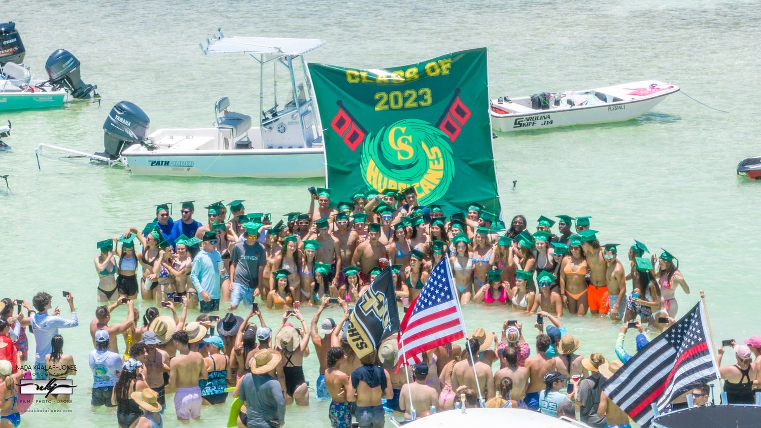 Large crowd gathered in water holding flags and a green banner during a boating event.
