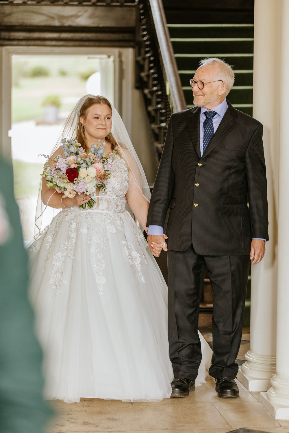 An elegant wedding moment showing a bride in a sparkling white gown and her escort walking together in a classic venue.
