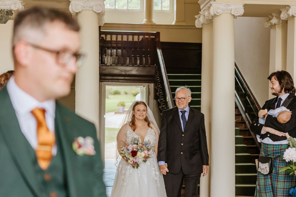 A wedding ceremony entrance at an elegant venue with stone columns as guests in formal attire prepare for the occasion.