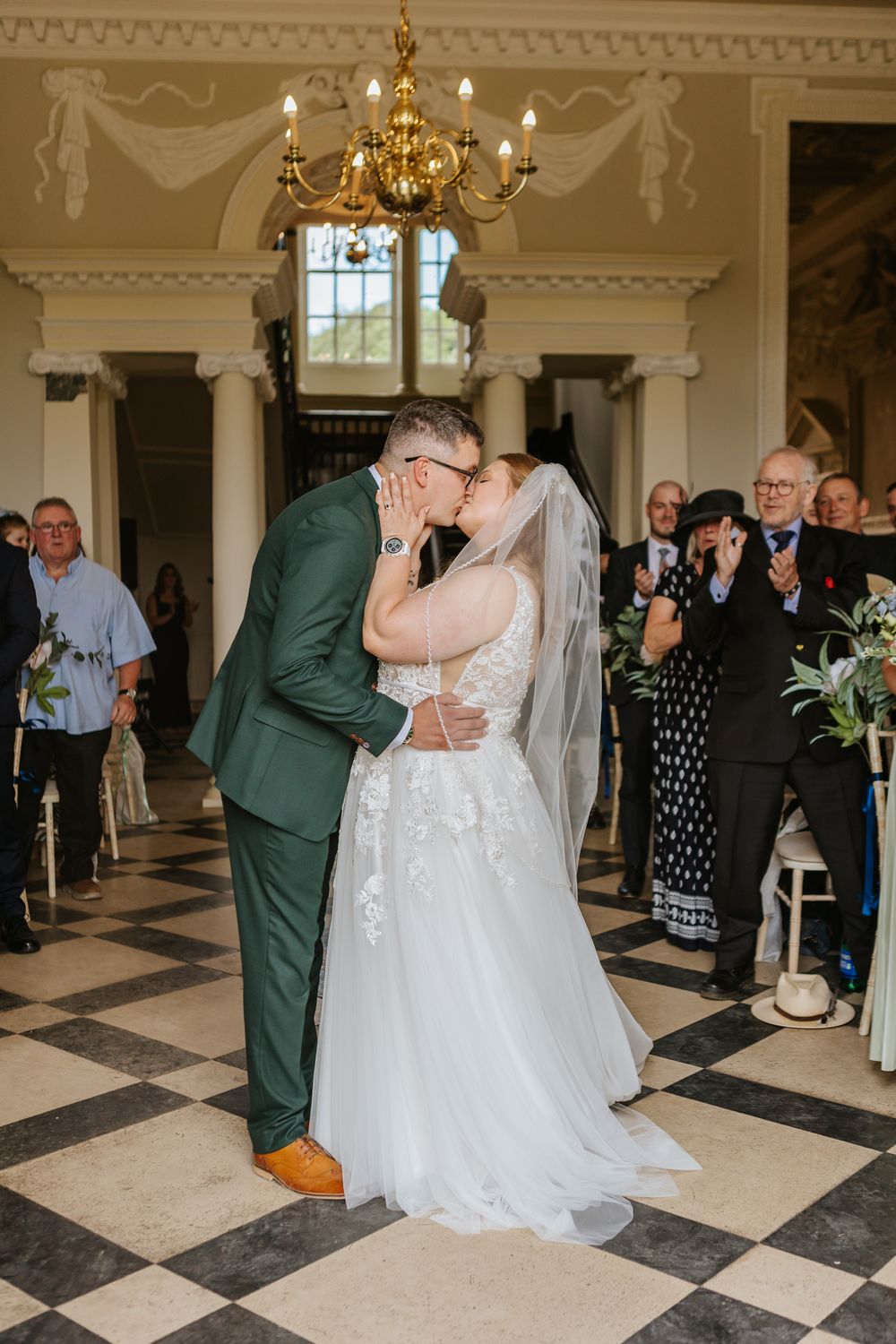 Couple dances together for their first dance in an elegant ballroom with checkered floors and ornate chandeliers.