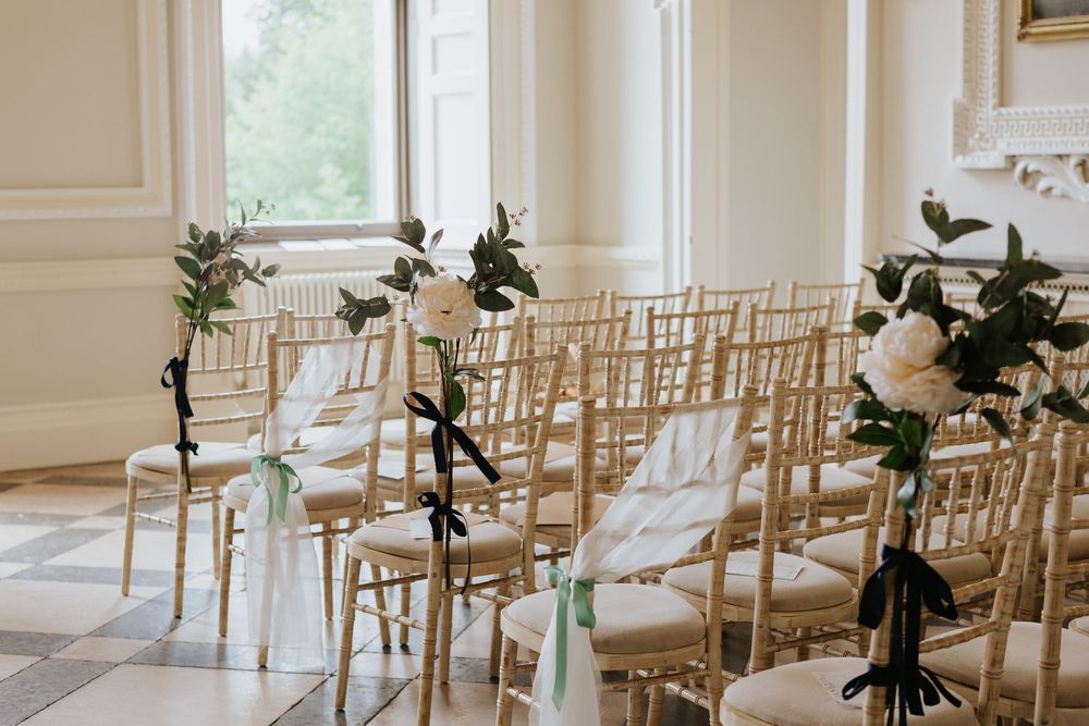 Gold chiavari chairs arranged in rows for an elegant indoor wedding ceremony with white floral decorations.