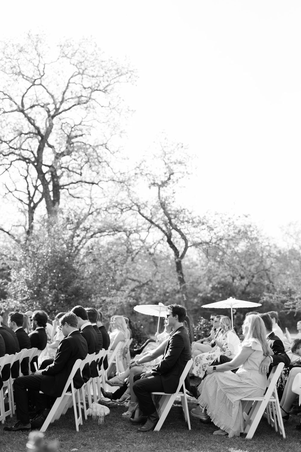 Guests seated in white folding chairs at an outdoor garden ceremony with bare winter trees in the background.
