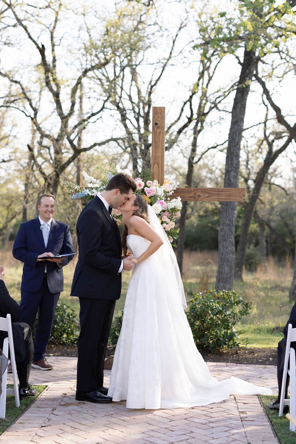 A couple shares a romantic moment at an outdoor wedding ceremony with a wooden cross and natural backdrop.