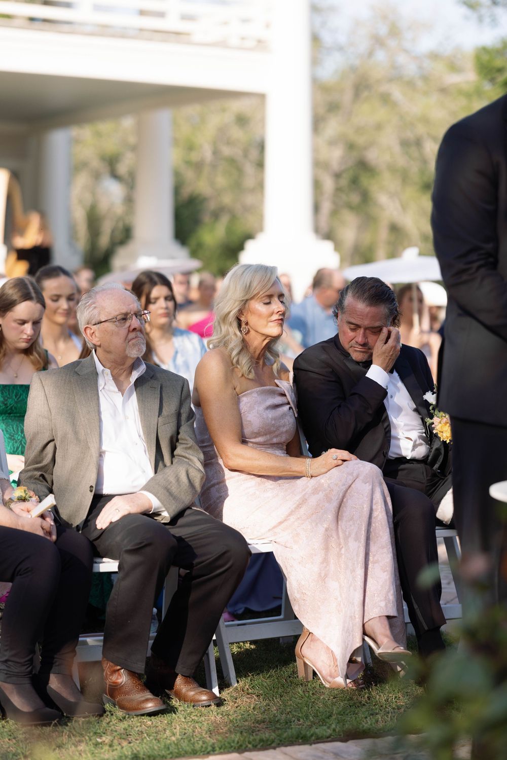 Guests seated on chairs in a grassy outdoor setting during what appears to be a wedding ceremony.