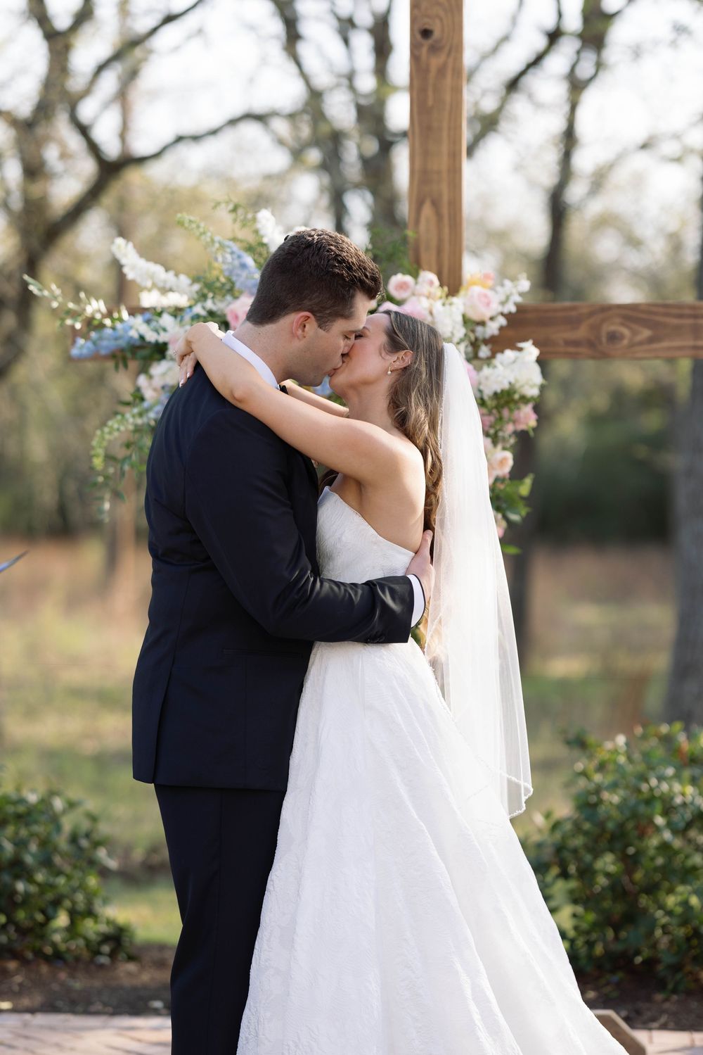 A bride and groom share their first kiss during their romantic outdoor wedding ceremony with floral decorations.