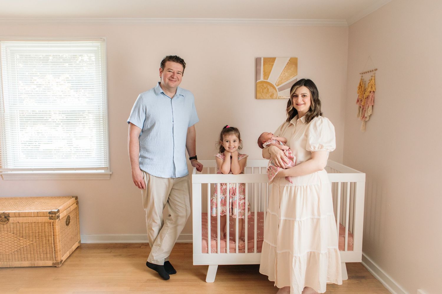 Family sits on floor of nursery with decorative floral wallpaper reading books together during a lifestyle newborn session in South Buffalo.