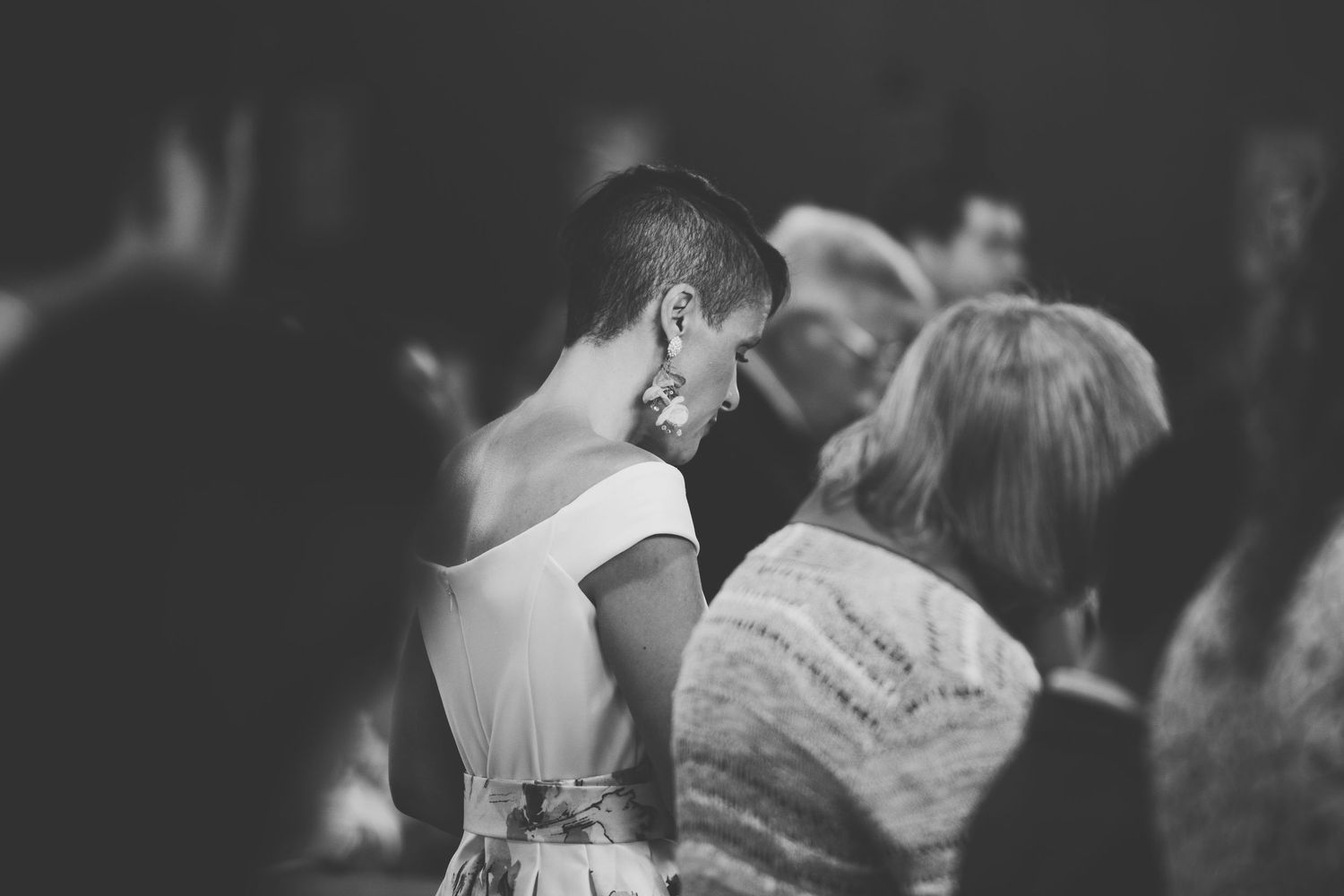 A black and white photograph shows people with their heads bowed in prayer during a catholic mass.