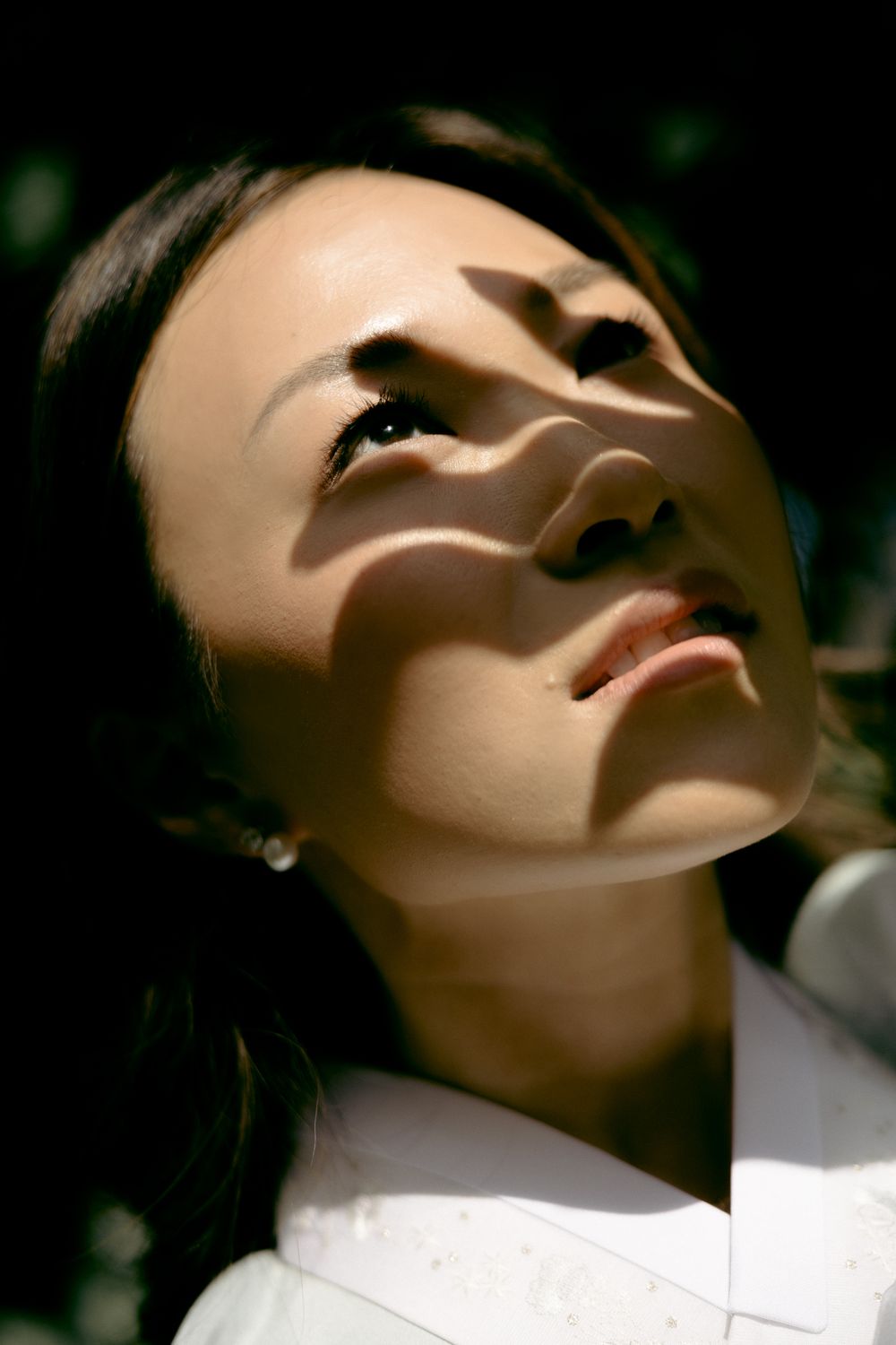 An artistic portrait with dappled light and shadows across a face against a dark background. Athens wedding photographer