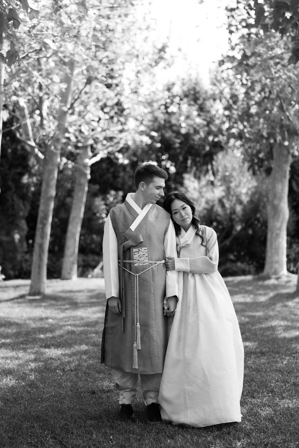 A romantic black and white photo of a couple in traditional Korean dress standing among trees. Athens wedding photographer