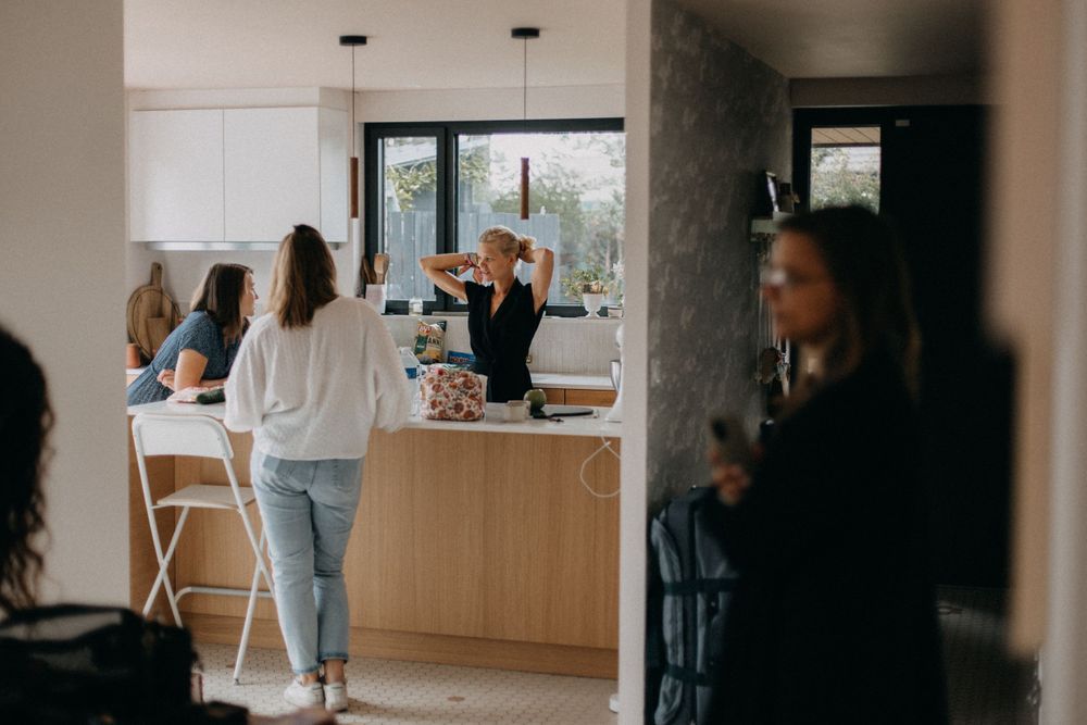 A bright modern kitchen scene with people gathering around a counter in casual conversation.
