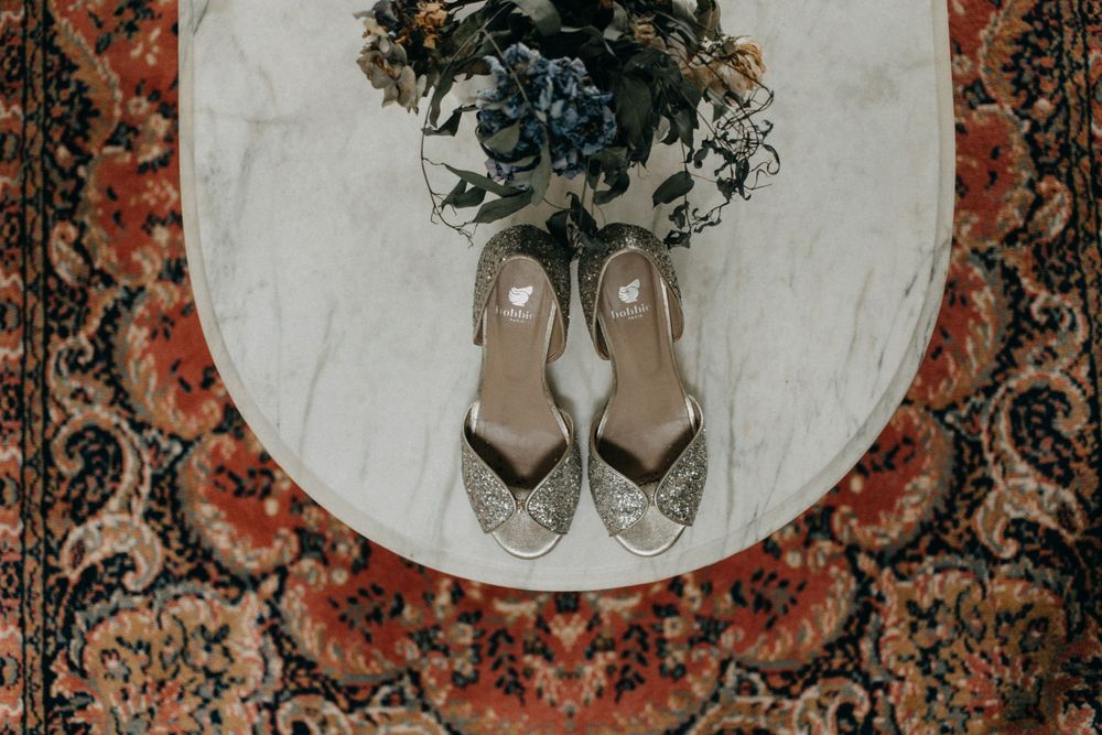 Silver shoes placed on round marble table with ornate rug underneath.