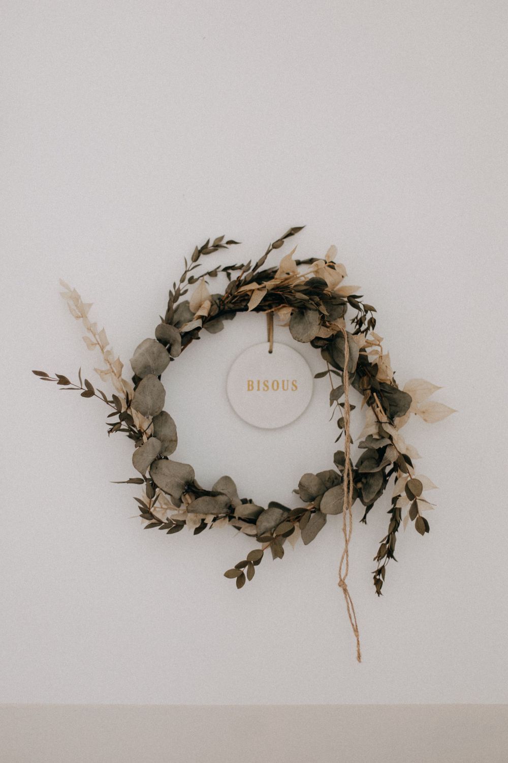 A minimalist eucalyptus wreath with dried flowers and a subtle 'Birds' tag hanging on a light gray wall.