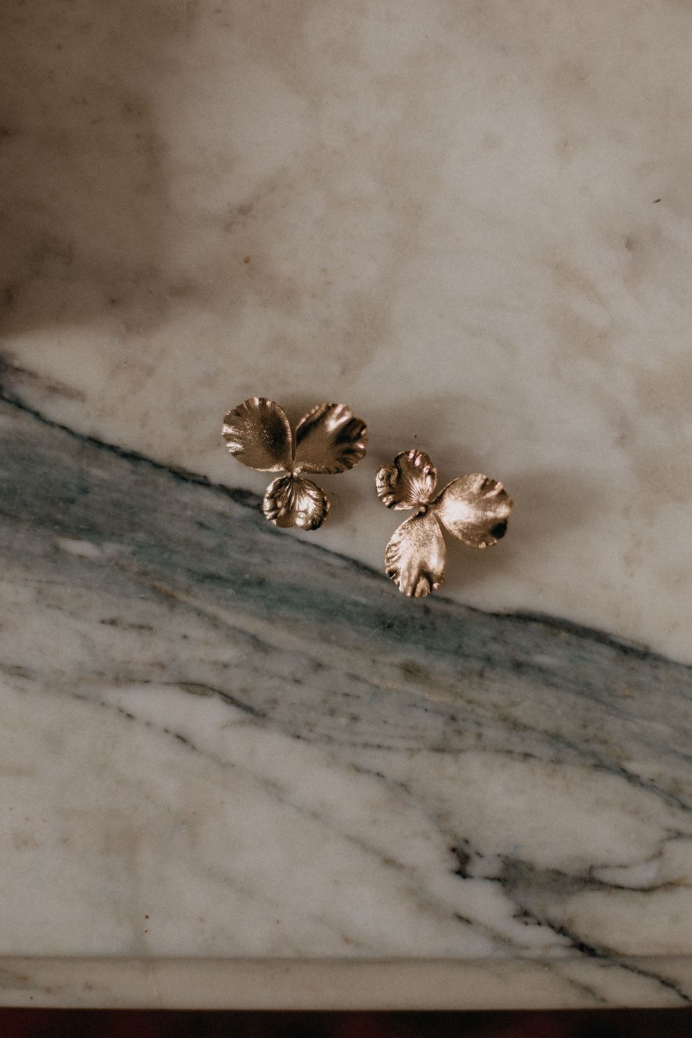 Gold floral-shaped earrings displayed on a marble surface with delicate details.