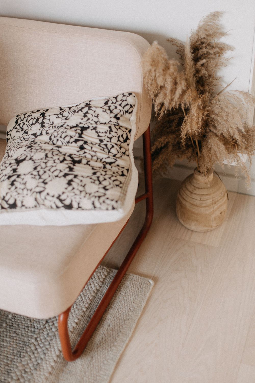 Modern rocking chair with patterned pillow and dried pampas grass in ceramic vase.