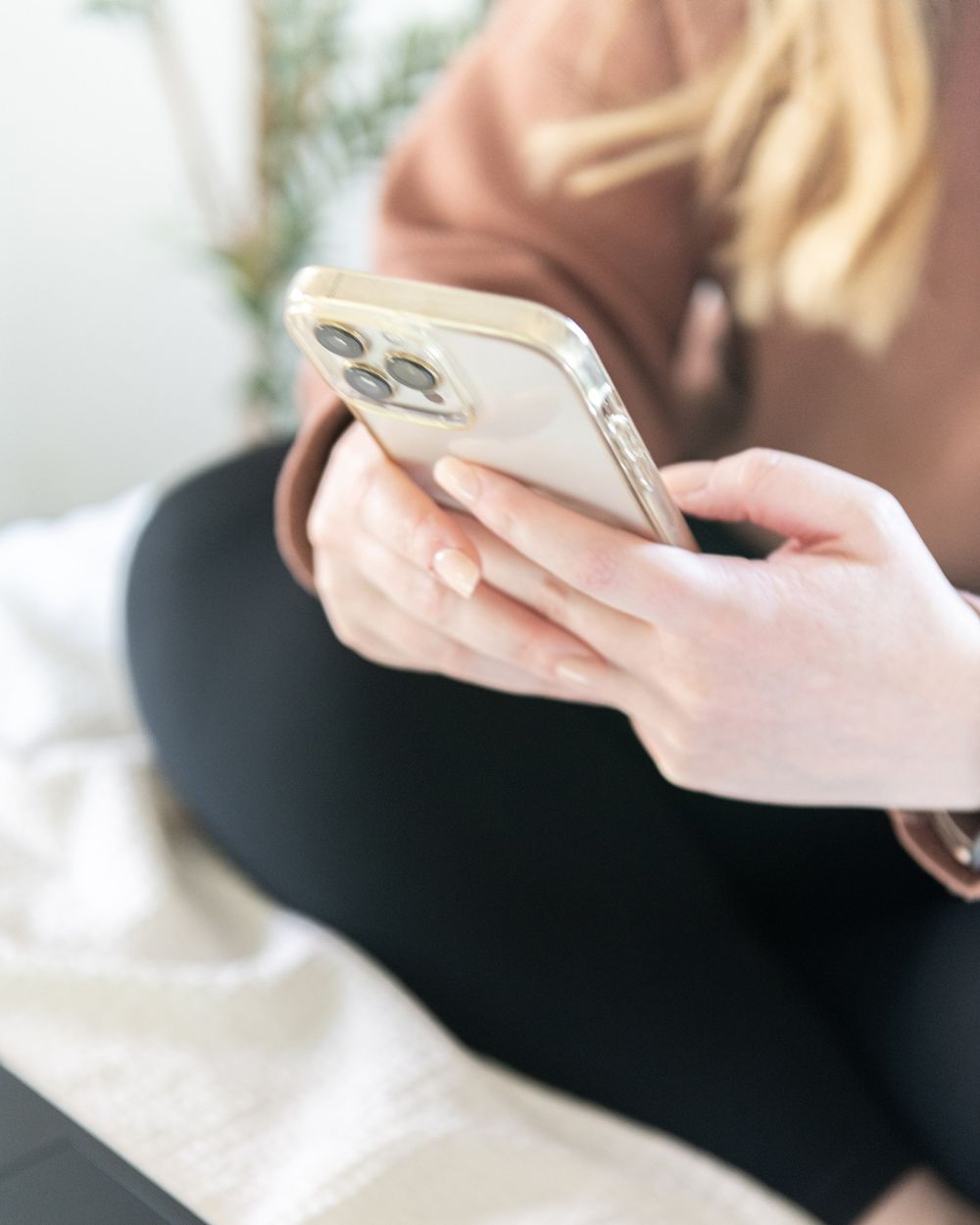 Close-up of hands holding iPhone showing camera system against white bedding.