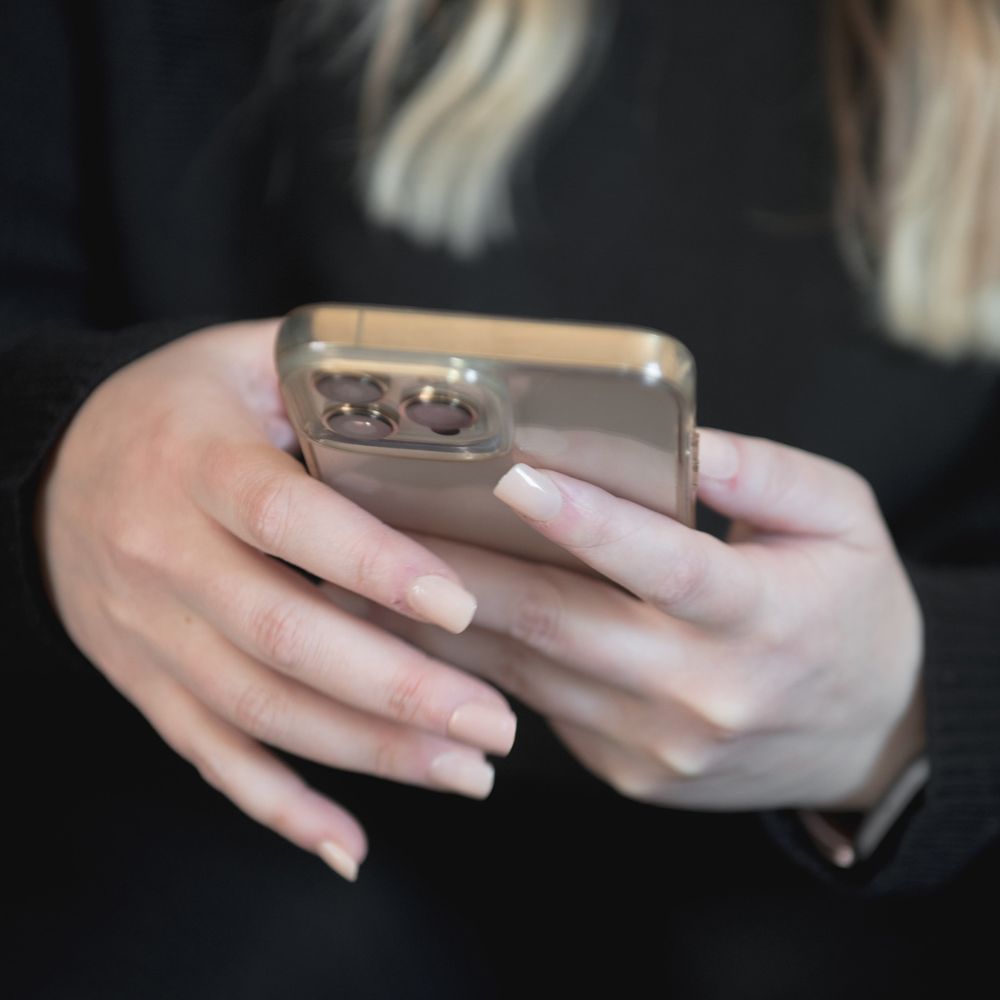 Close-up of hands with manicured nails holding a gold iPhone while texting.