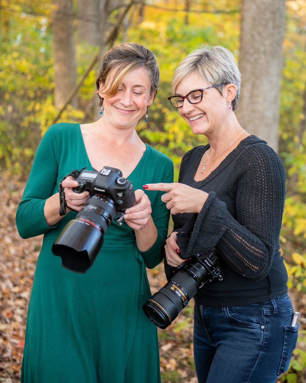 Two photographers reviewing photos on their cameras in an autumn forest setting.