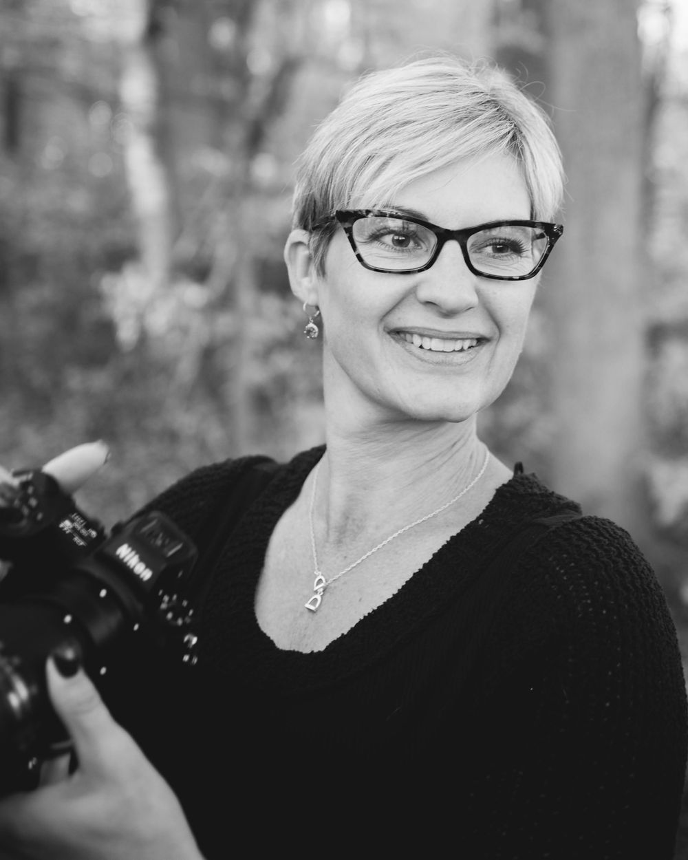 Portrait of photographer wearing cat-eye glasses and black sweater while holding professional camera.