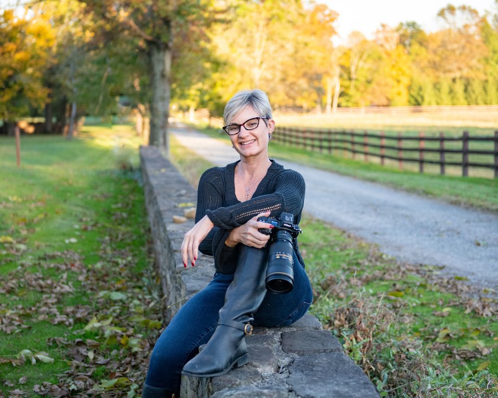 Photographer sitting on rustic fence post along country path during golden hour.