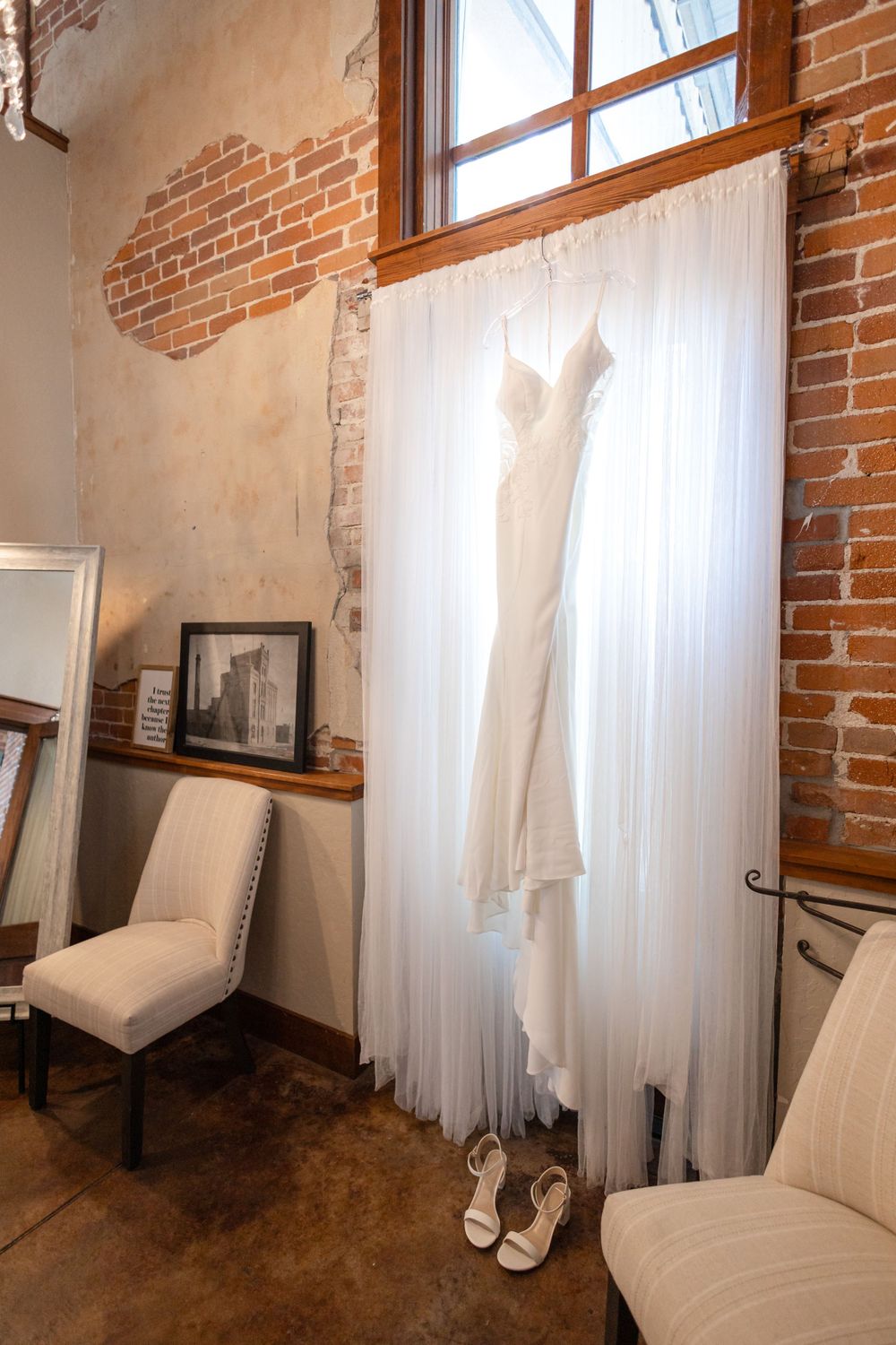 Wedding dress silhouette against white curtain in rustic brick room with vintage decor.