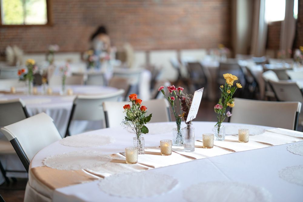 Wedding reception table setup with white linens and simple floral centerpieces.