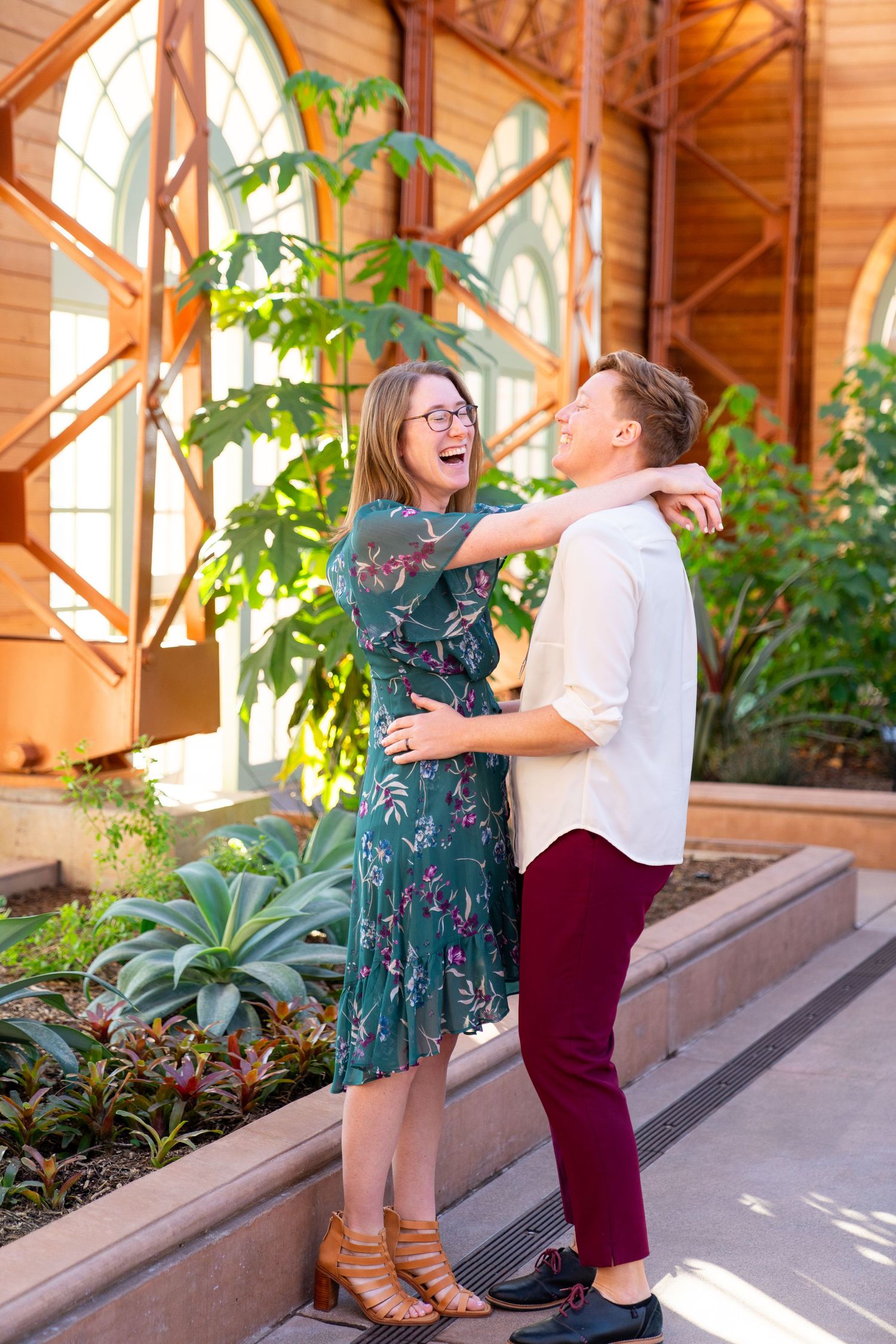 Happy couple sharing a joyful moment together in a sunlit indoor garden space with large windows and tropical plants.