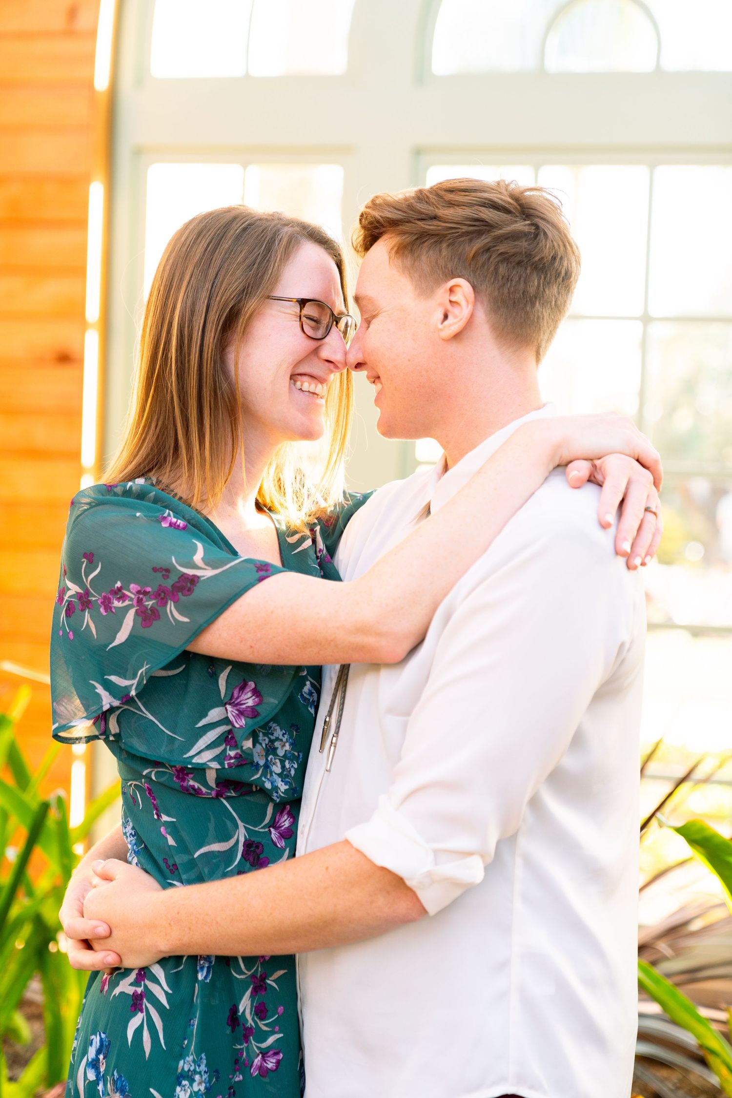 A romantic couple embraces and shares a close intimate moment in a sunlit room with indoor plants.