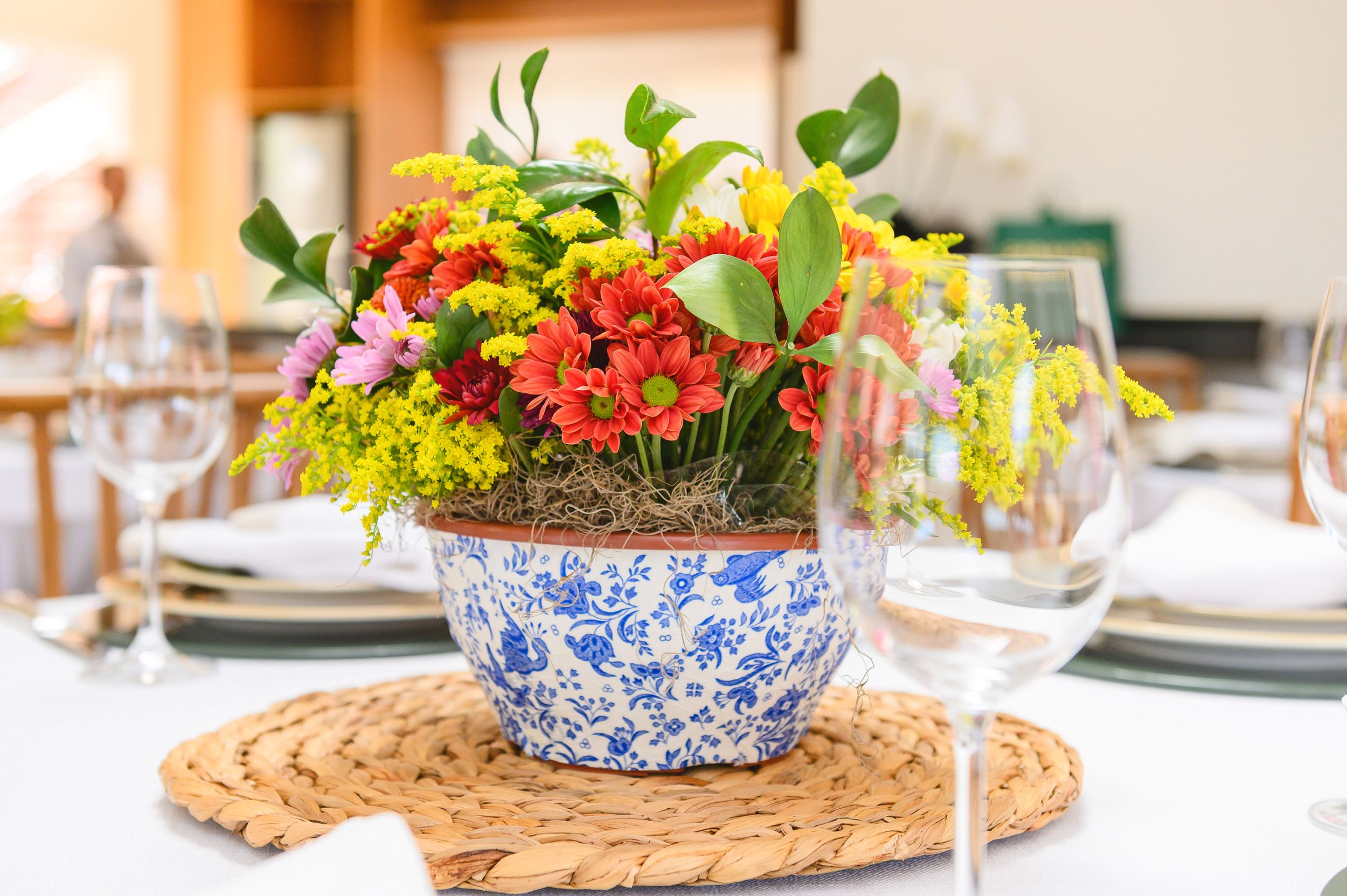Fresh floral centerpiece arrangement in blue and white chinoiserie vase on woven placemat at elegant table setting.
