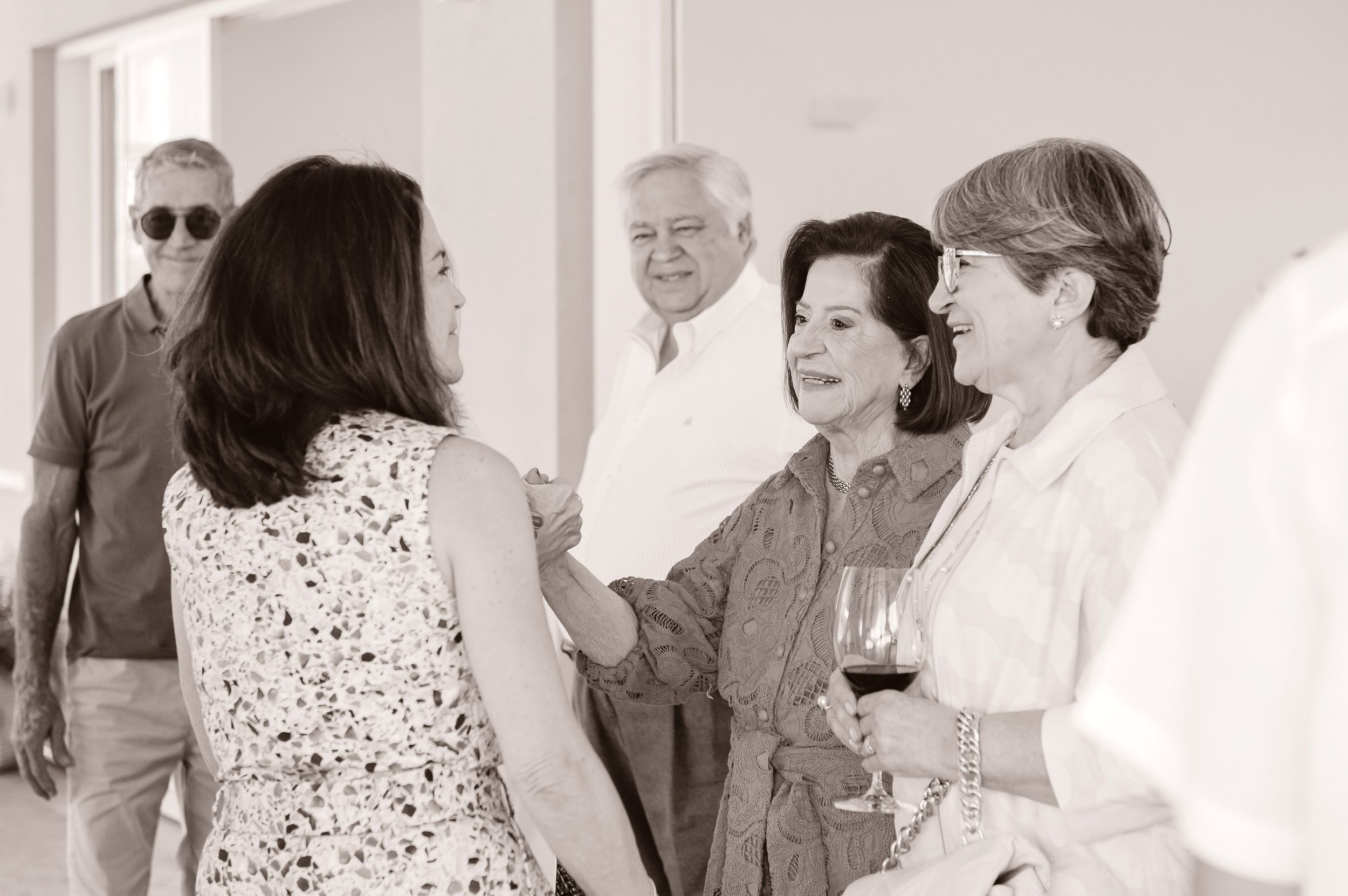 A group of people conversing at a social gathering while holding wine glasses in a bright interior space.