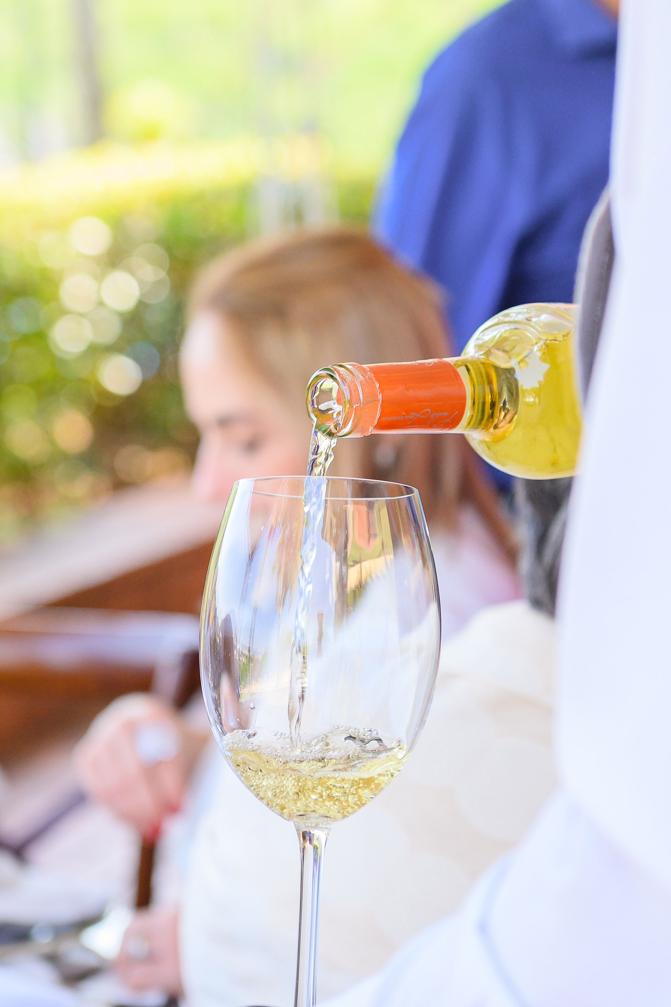 White wine being poured into an elegant wine glass at an outdoor dining table.