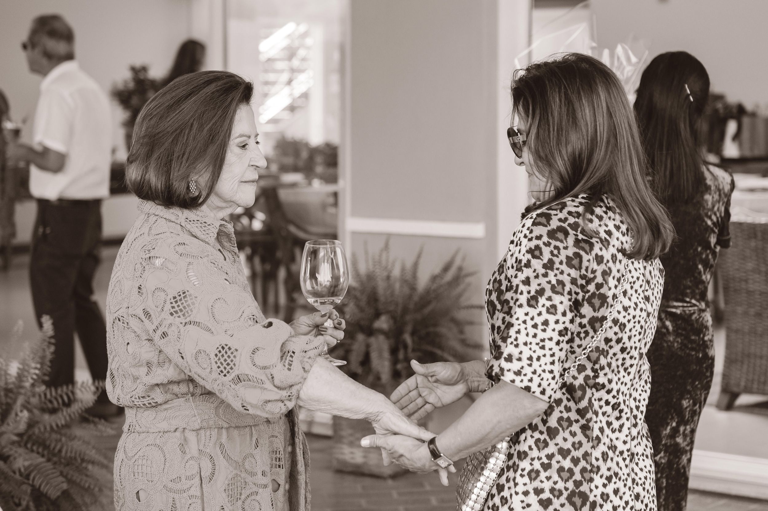 People mingling at an indoor social gathering in black and white, with someone wearing a leopard print dress among guests.
