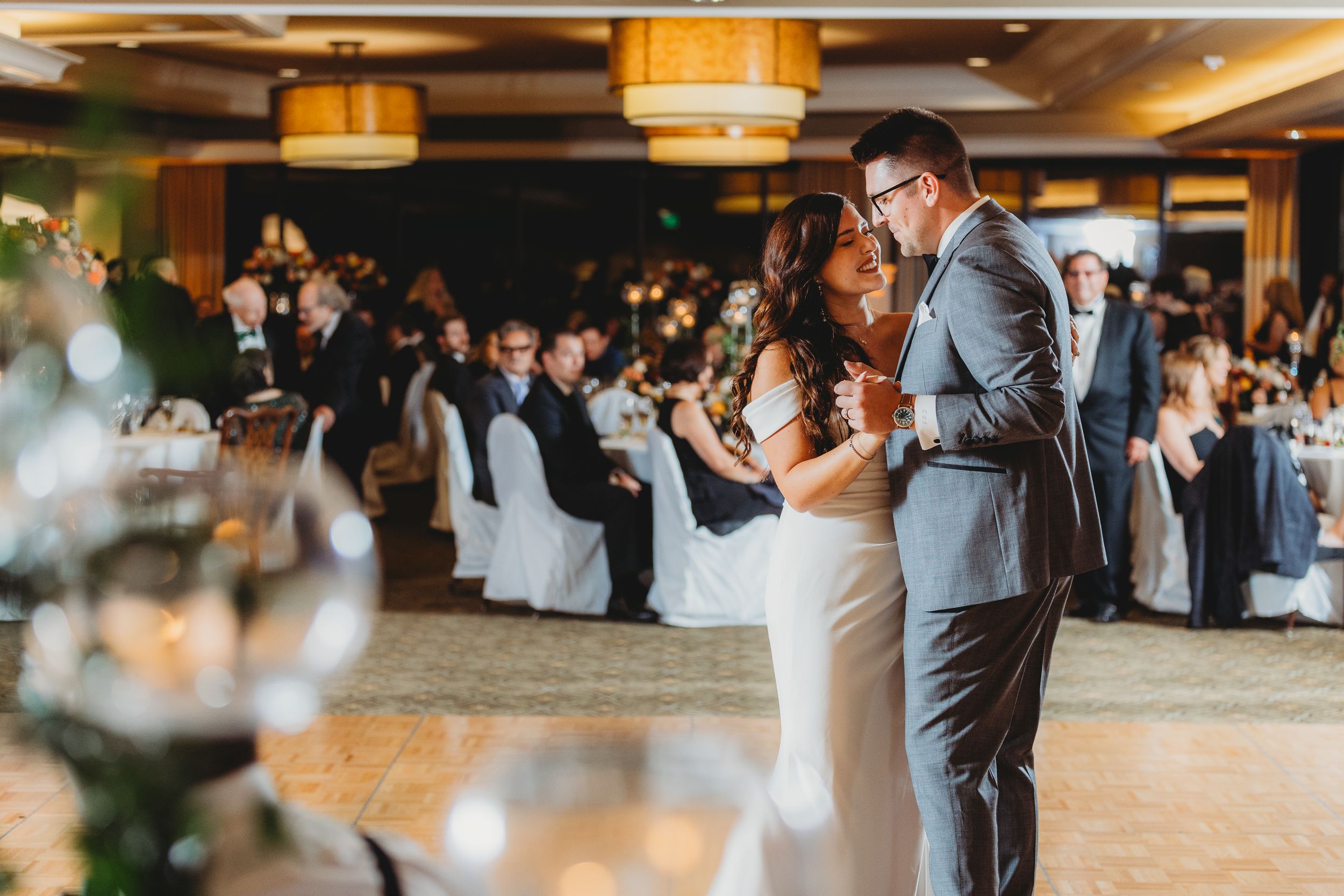 Dancing couple shares intimate moment during first dance at elegant indoor wedding reception with guests watching.