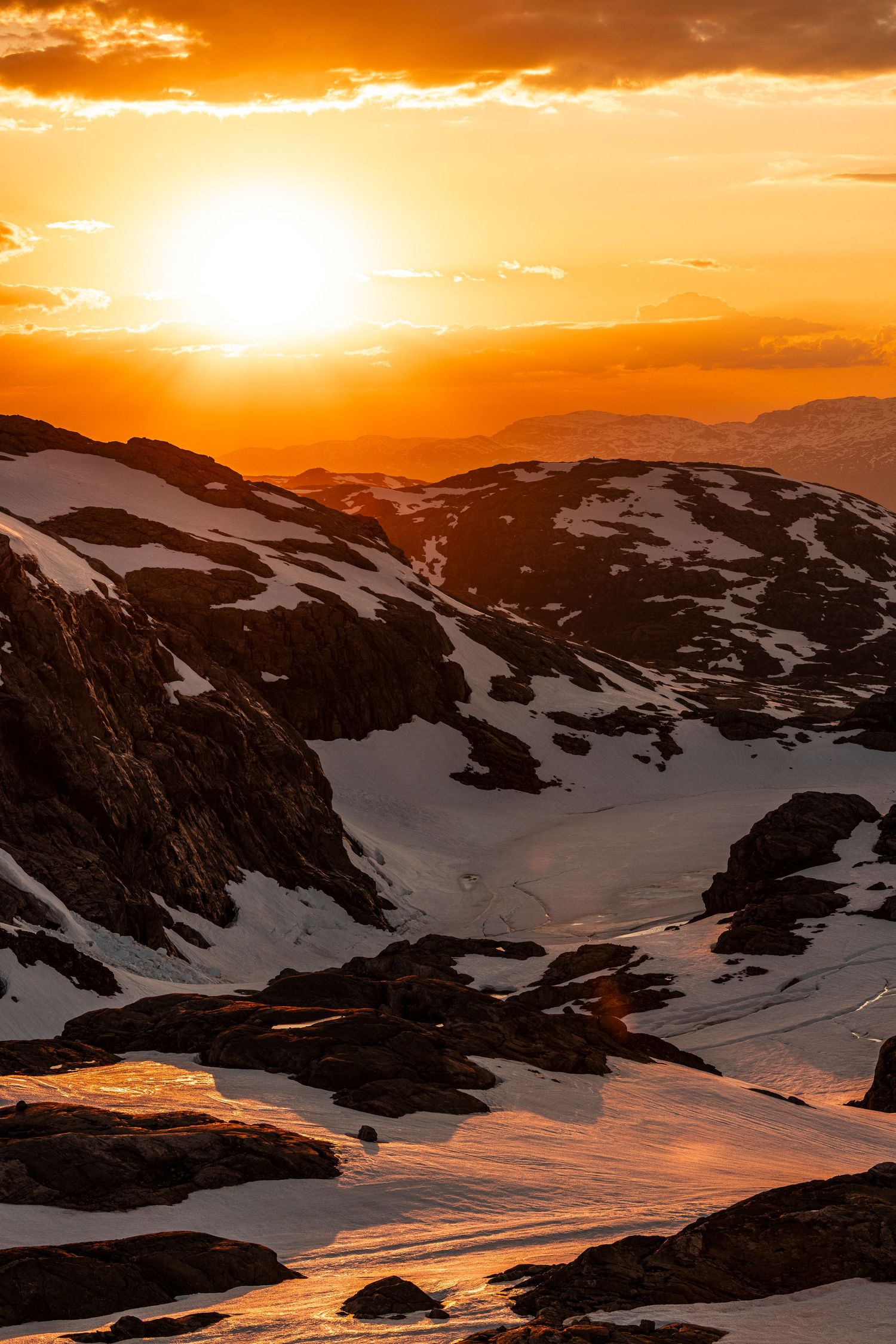 Snow-covered mountain peaks bathed in golden light at sunset with dramatic orange sky overhead.