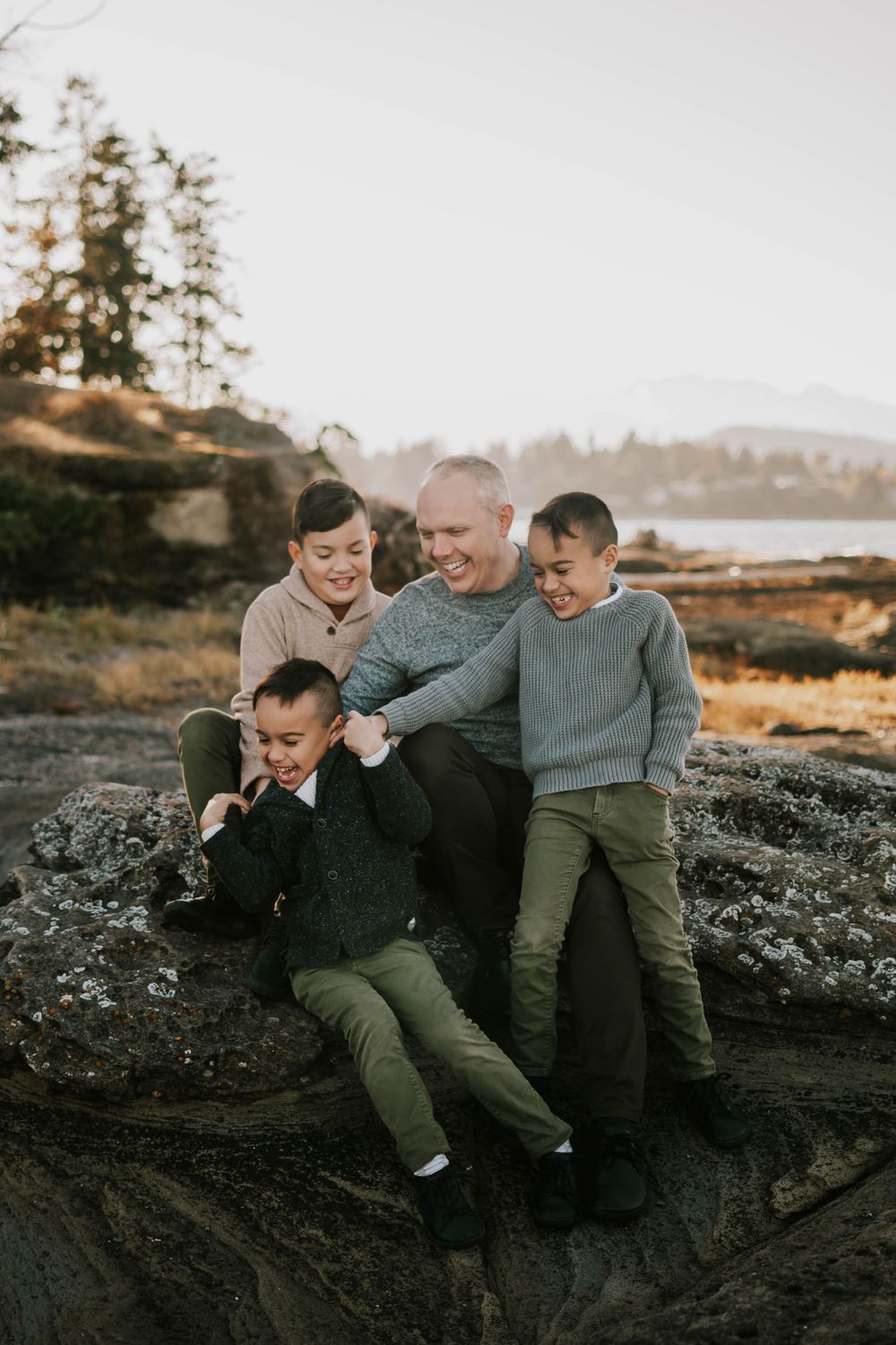 Beautiful soulfull photography of dad and sons sitting on Madrona Point beach's rocky shore on Vancouver Island during golden hour