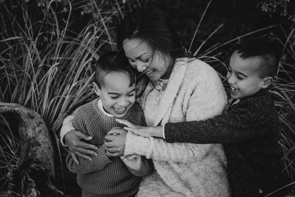 Beautiful soulfull portrait photography of mom hugging sons on Madrona Point beach's rocky shore on Vancouver Island during golden hour