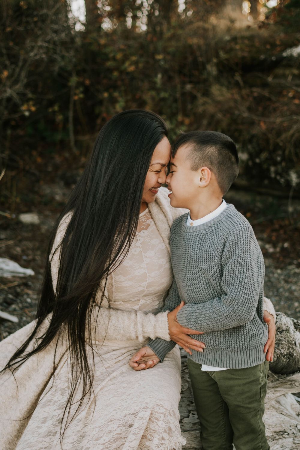 Cute mother and son portrait photography of family sitting on Madrona Point beach's rocky shore on Vancouver Island during golden hour