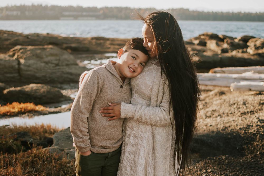 Parksville photographer portrait of mom hugging with young sons on Madrona Point beach's rocky shore and laughing on Vancouver Island
