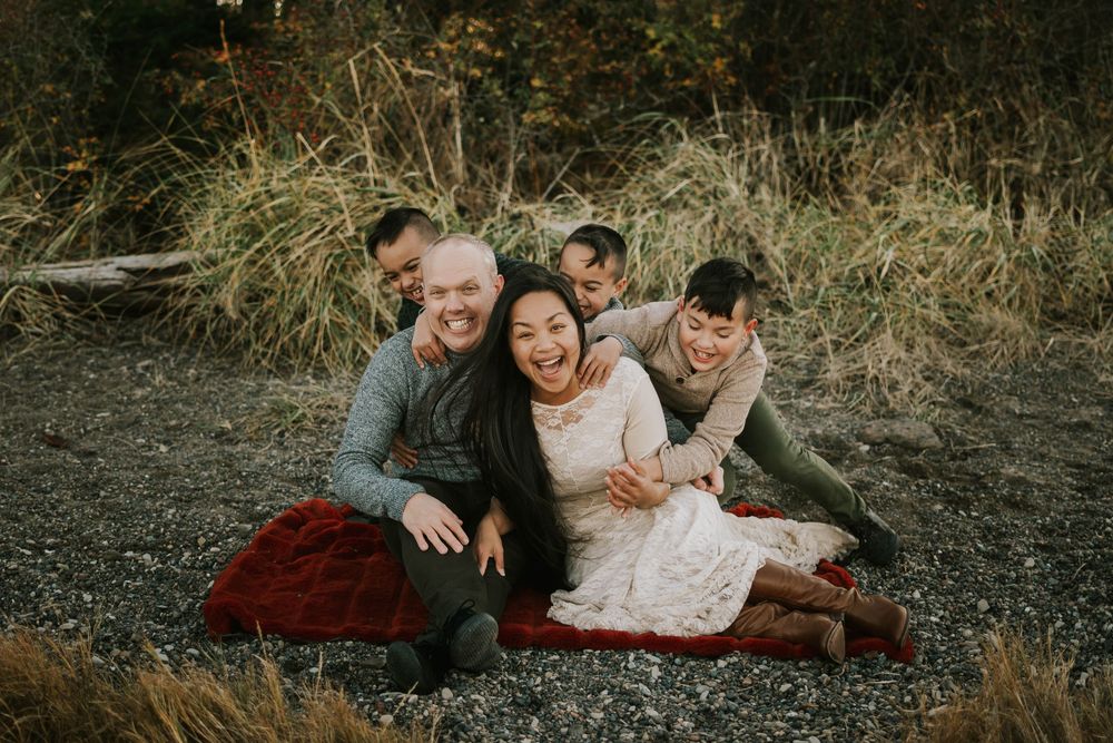 Parksville photographer portrait of family sitting on Madrona Point beach's rocky shore and laughing on Vancouver Island