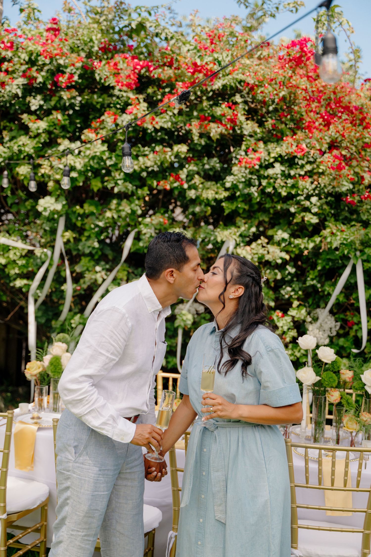 A romantic celebration set against vibrant bougainvillea with champagne glasses and elegant party decor in a garden setting.