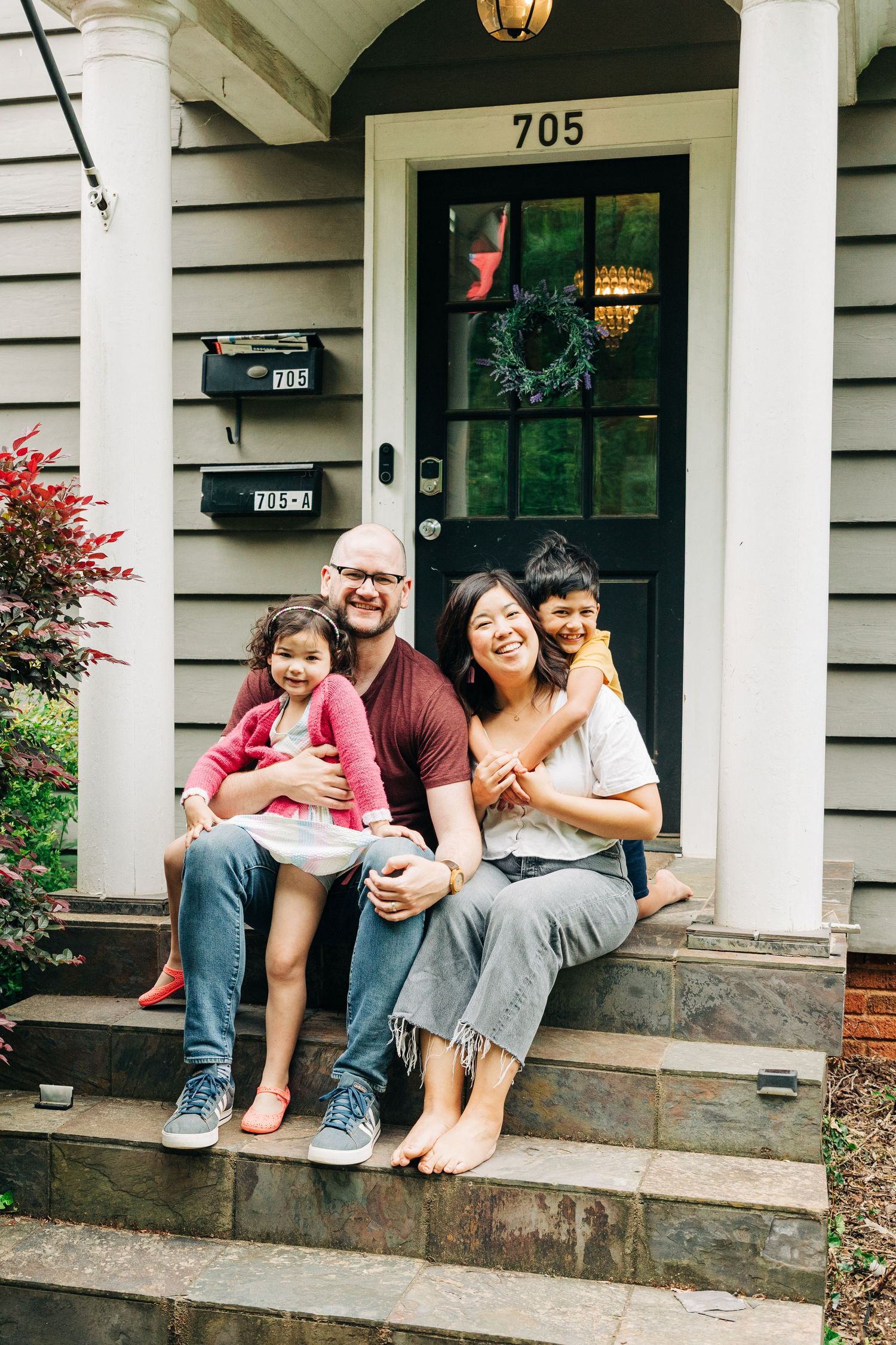 A cozy front porch scene of a family with brick steps, white columns, and a dark door under a hanging lantern in Charlotte, NC